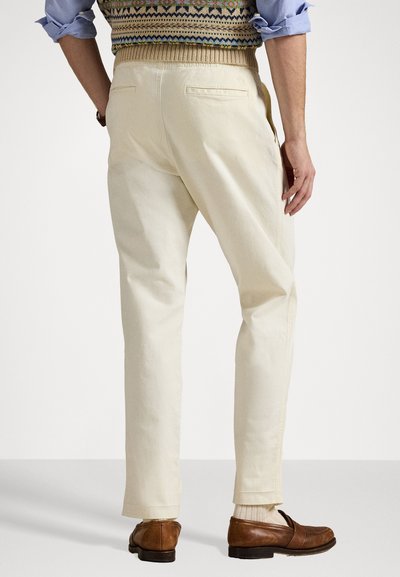 Pantaloni din bumbac bej cu un design drept, având buzunare la spate și tiv cu mansete, purtați cu pantofi din piele maro.