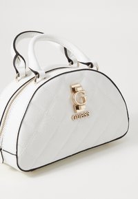 Borsa a tracolla bianca trapuntata con bordi neri, caratterizzata da doppi zip e un accento logo in tono oro sul fronte. Forma compatta e arrotondata.