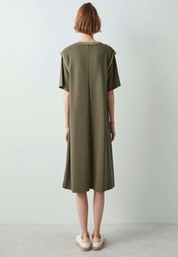 Khaki green knee-length dress, short sleeves, clean lines, soft texture, rounded neckline, contrasting stitching details, paired with light footwear.