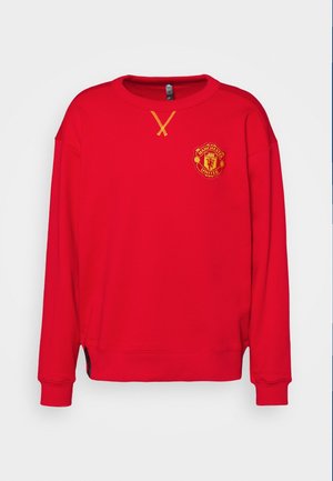 Sweat-shirt rouge à manches longues avec le logo de Manchester United sur la poitrine et un détail cousu jaune sous l'encolure.