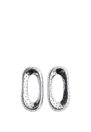 Deux boucles d'oreilles ovales en argent poli avec des bords irréguliers et de petits trous perforés sur toute leur surface.