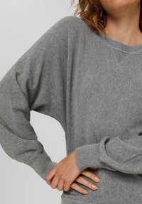 Pull gris surdimensionné avec un col rond, des poignets côtelés et une texture lisse. Caractéristiques : coupe décontractée et coutures d'épaule tombantes.