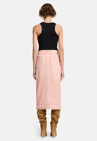 Jupe en denim rose longue avec poches arrière, coupe droite, et détails de couture visibles, associée à un débardeur noir ajusté et des bottes hautes beige.