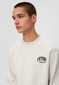 Hellgrauer Pullover mit Rundhalsausschnitt, auf der linken Brust mit schwarzem Text "FUTURE VISUALS" versehen. Weiche Textur, lässige Passform.