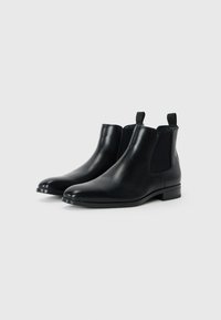 Botas Chelsea de piel negra con paneles laterales elásticos y tiradores. Textura suave, punta redondeada y diseño minimalista. Tacón plano.