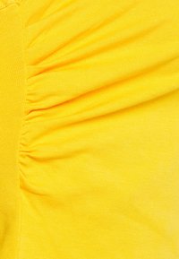 Close-up of yellow fabric with gathered, ruched detailing creating textured folds.