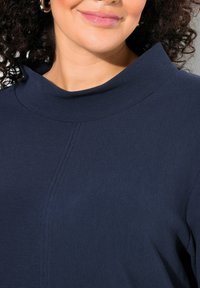 Navyblaues, geripptes Oberteil mit hohem Kragen und einer Nahtdetails. Glatte Textur mit fester Silhouette, ideal zum Schichten.