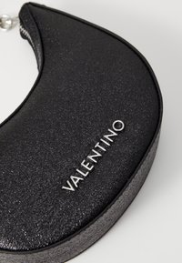Clutch in pelle nera con superficie texture, forma curva, dettaglio in argento della cerniera e logo "Valentino" in rilievo sul davanti.