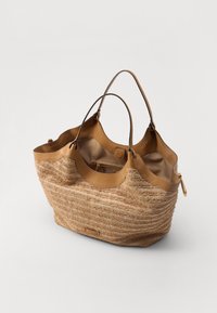 Sac fourre-tout en paille tressée marron avec deux poignées en cuir, fermeture éclair et poche intérieure. Présente une surface texturée et un design contourné.
