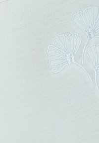 Tissu bleu clair avec une texture lisse, arborant une broderie délicate bleu clair de motifs floraux dans le coin.