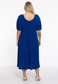 Blauwe midi-jurk met korte puffmouwen, geplooide achterkant, gladde textuur en een brede ronde halslijn. Draag het met witte haksandalen.