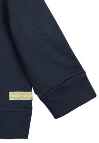 Maglietta a maniche lunghe blu navy con polsini a coste e un'etichetta con "loud + proud" in giallo sull'orlo inferiore. Tessuto morbido, design semplice.