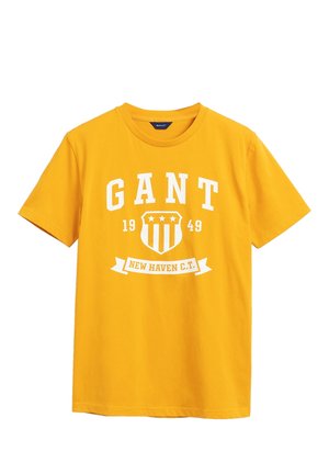 Gul T-shirt med korte ærmer med hvidt tryk med teksten "GANT 1949" og et skjoldlogo over banneret "NEW HAVEN C.T." på brystet.