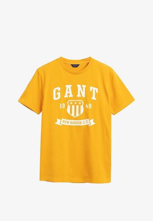 Gelbes T-Shirt mit kurzen Ärmeln und weißem Aufdruck mit der Aufschrift „GANT 1949“ und einem Schild-Logo über dem Banner „NEW HAVEN C.T.“ auf der Brust.