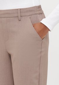 Pantalons beige clair avec une texture subtile, dotés d'une taille élastique et de poches latérales. Coupe droite avec des coutures nettes.