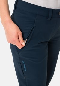 Pantalons de randonnée bleu marine en tissu doux, dotés d'une poche zippée sur la cuisse et d'un logo visible sur le côté.