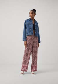 Giacca di jeans con una vestibilità cropped, abbinata a pantaloni larghi floreali nei toni rosa e bianco, con un motivo e un orlo a contrasto. Sandali platform bianchi.