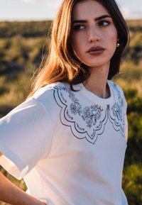 Witte t-shirt met een scalloped zwart geborduurd col met bloemdesigns. Korte mouwen en een relaxed fit.