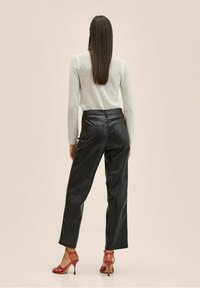 Pantalones de cuero sintético negros con un ajuste holgado, cintura alta y bolsillos traseros visibles, combinados con tacones rojos con tiras y un suéter gris claro.