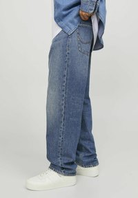 Blaue Denim-Jeans mit lockerer Passform, mit distressed Details und einem 5-Taschen-Design, kombiniert mit weißen Sneakers.