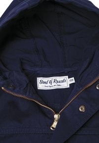 Granatowa kurtka z wnętrzem z złotym zamkiem, detalami w przeszyciach i metką z napisem "Band of Rascals" oraz informacjami o organicznej odzieży dziecięcej.