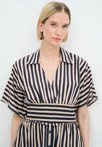 Vestido a rayas con escote en V profundo, mangas cortas y cintura elástica. Presenta rayas en azul marino y beige y detalle de botones en la parte delantera.