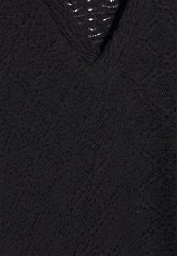 Tissu en dentelle noire avec des motifs floraux et une petite ouverture en V au niveau du col.