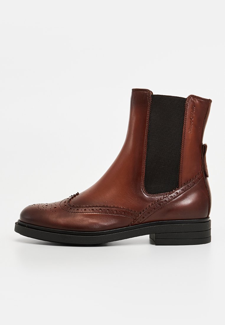 Braune Lederstiefeletten mit Brogue-Design, elastischen Seitenpaneelen und einer flachen schwarzen Gummisohle. Glatte Textur mit Verzierungen entlang der Kanten.