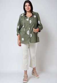 Olijfgroene blouse met witte bloemenborduursels, knoopsluiting aan de voorkant, geplooide halslijn en driekwart mouwen. Gecombineerd met crèmekleurige cropped broeken en beige wedgesandalen.