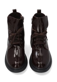 Brązowe lakierowane botki ze skóry z gładkim wykończeniem, z przodu wiązane na sznurowadła, z paskiem wokół kostki i bocznym zamkiem błyskawicznym. Czarna teksturowana podeszwa.