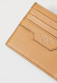 Tan textured leather cardholder with multiple card slots and silver "Lancel Paris" logo on a plain white background.