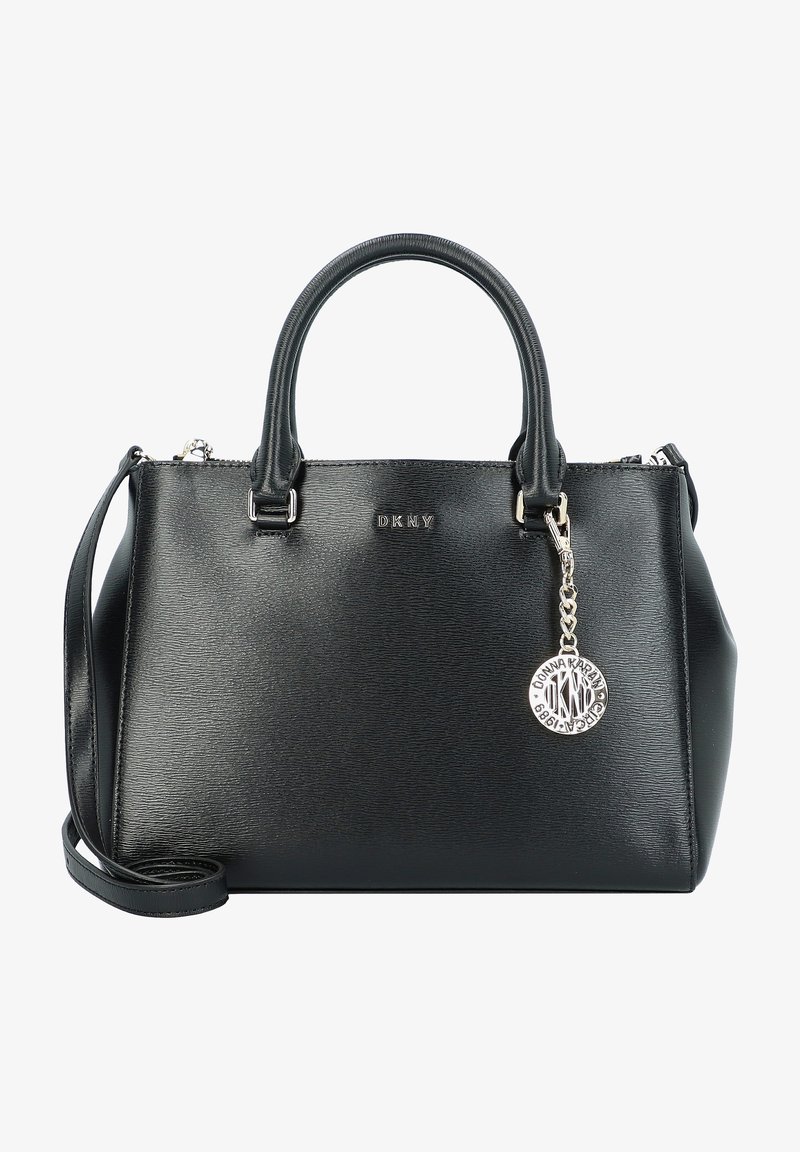 Sac à main DKNY en cuir noir avec deux poignées, bandoulière amovible et breloque ronde argentée avec logo à l'avant.
