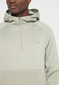 Jasnozielony polar na zamek z kapturem, z teksturowanym wzorem, posiadający logo na piersi oraz praktyczną kieszeń typu kangur.