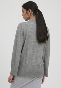 Pulover gri din tricot, cu mâneci lungi și un guler înalt, având o croială lejeră și detalii fine cu nervuri la margine.