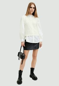 Witte gebreide vest over een blouse, gecombineerd met een zwarte leren rok. Zwarte combat boots en een kleine zwarte tas met studs.