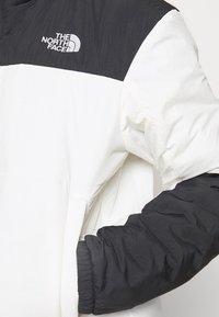 Czarna i biała kurtka North Face z zamkiem przy kołnierzu, elastycznymi mankietami oraz gładkim, lekkim materiałem z logo na górnej lewej stronie.