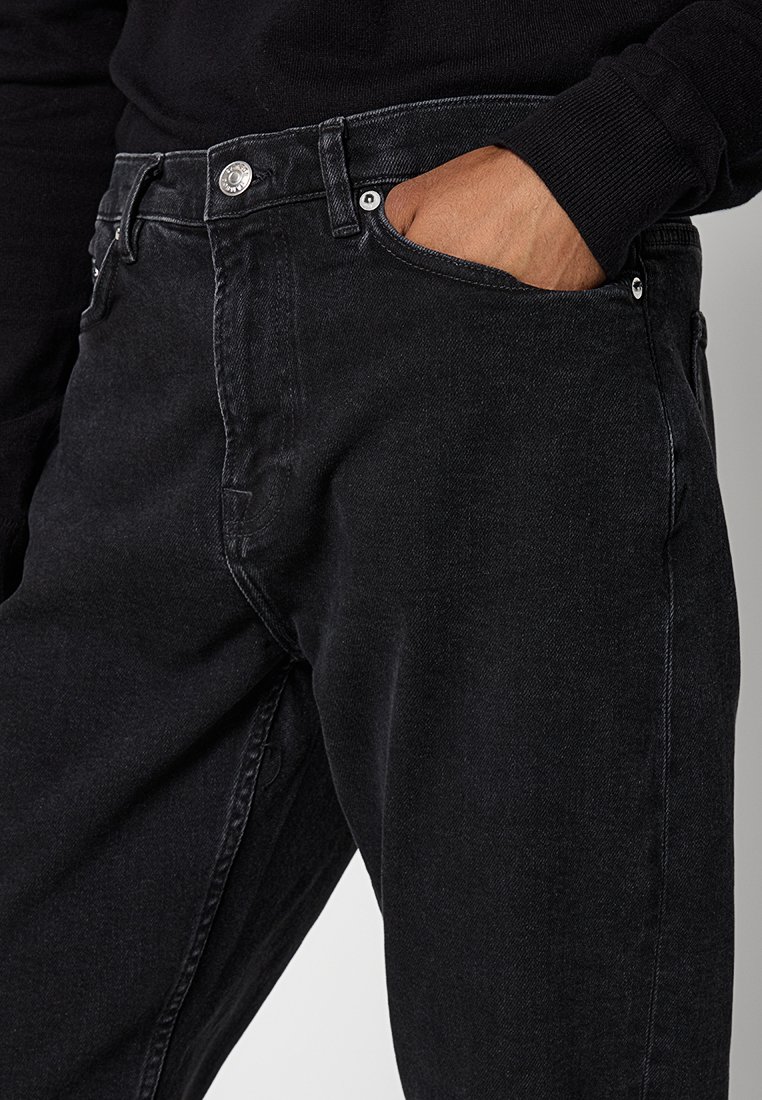 Czarne dżinsy o dopasowanym kroju, pięciokieszeniowym wzorze, z metalowym zapięciem i subtelnymi detalami w szwie. Teksturowana tkanina wydaje się być trwała.