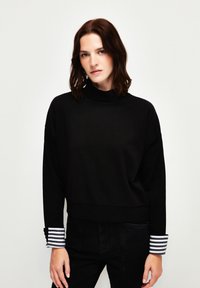 Schwarzer Sweatshirt mit hohem Kragen, fallenden Schultern und kontrastierenden gestreiften Bündchen. Weicher Stoff mit lockerer Passform und minimalen Nähten.