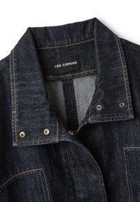 Dark blue denim jacket collar with orange stitching and metal snap buttons, featuring a black label with white text "LES COPAINS".