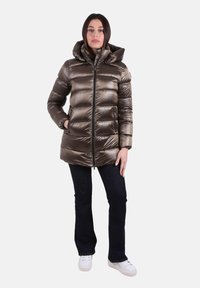 Gewatteerd bruin jack met capuchon, ritssluiting aan de voorkant, twee zijzakken en geribbelde boorden; gecombineerd met een donkere spijkerbroek en witte sneakers.