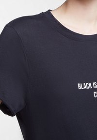 Černé tričko, krátké rukávy, kulatý výstřih, měkká tkanina, na přední straně bílé písmo "BLACK IS", bezšvové ramena.