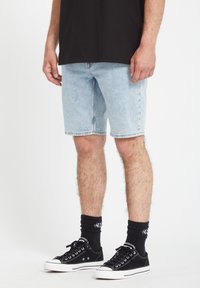 Lyseblå denimshorts med lige snit, båret med sorte sneakers og ankelstrømper. Har et enkelt design og en frynset kant.