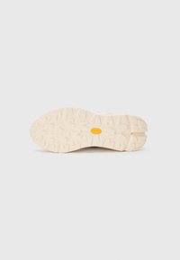 Rubber sneaker outsole with a textured pattern, featuring a light beige color and a yellow octagonal logo at the center.