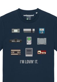 Navy blue t-shirt featuring eight pixelated video game consoles and cartridges, with the text "I'M LOVIN' IT" in bold gray below.