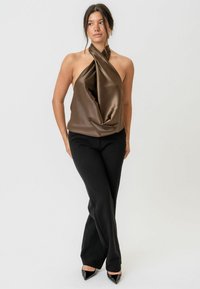 Brązowy satynowy top na halter z twisted dekoltem, zestawiony z czarnymi dopasowanymi spodniami oraz czarnymi czółenkami na szpilce. Gładka tekstura i nowoczesny design.