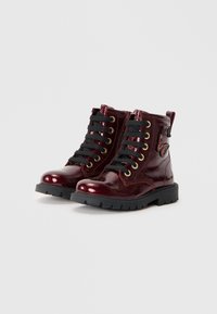 Bottines en cuir verni bordeaux avec des lacets noirs, des œillets dorés et une finition texturée. Semelle noire imposante et accents décoratifs sur le côté.