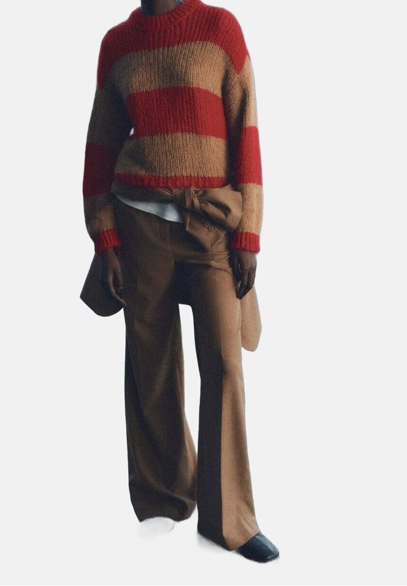 Personne portant un pull en tricot rayé rouge et beige, un pantalon large marron avec une ceinture nouée, et des chaussures noires à bout carré.