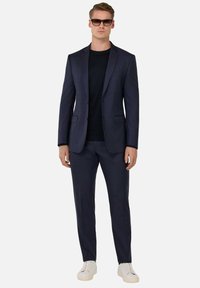 Navy suit with a textured pattern, tailored fit, single-button jacket, and matching trousers paired with a black t-shirt and white sneakers.