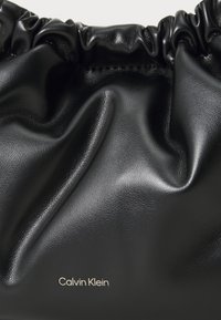 Borsa a mano in pelle nera con texture arricciata. Presenta un'iscrizione del logo in oro, una finitura liscia e angoli arrotondati.