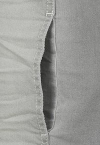 Grijze denim stof met een verticale naad en witte stiksels. De stof heeft een gladde textuur met lichte kreuken en een ruwe rand.